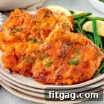 Two fried pork chops on a stack of small round plates. Pork chops are plated with green beans and a lemon wedge.