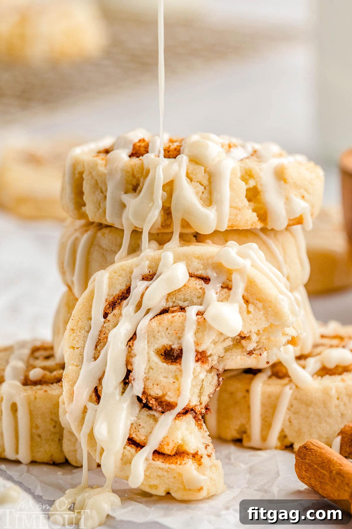 Cinnamon Swirl Delights 9 Cinnamon Roll Cookies with icing in a stack. One cookie is leaning on the stack with a bite taken. Icing is being drizzled onto the cookies.