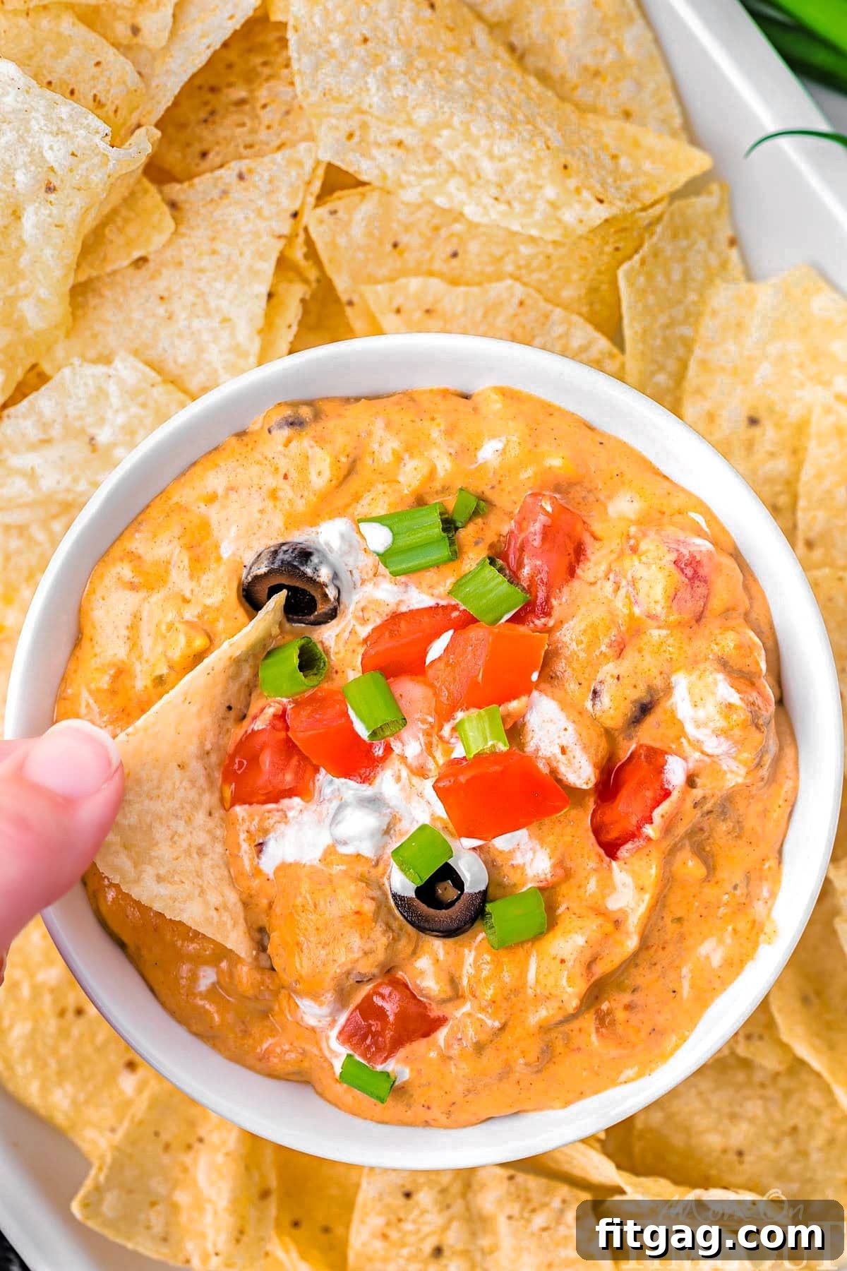 Warm and Cheesy Slow Cooker Taco Dip 6 A top down shot of a bowl of crockpot taco dip with a hand dipping a chip into it.