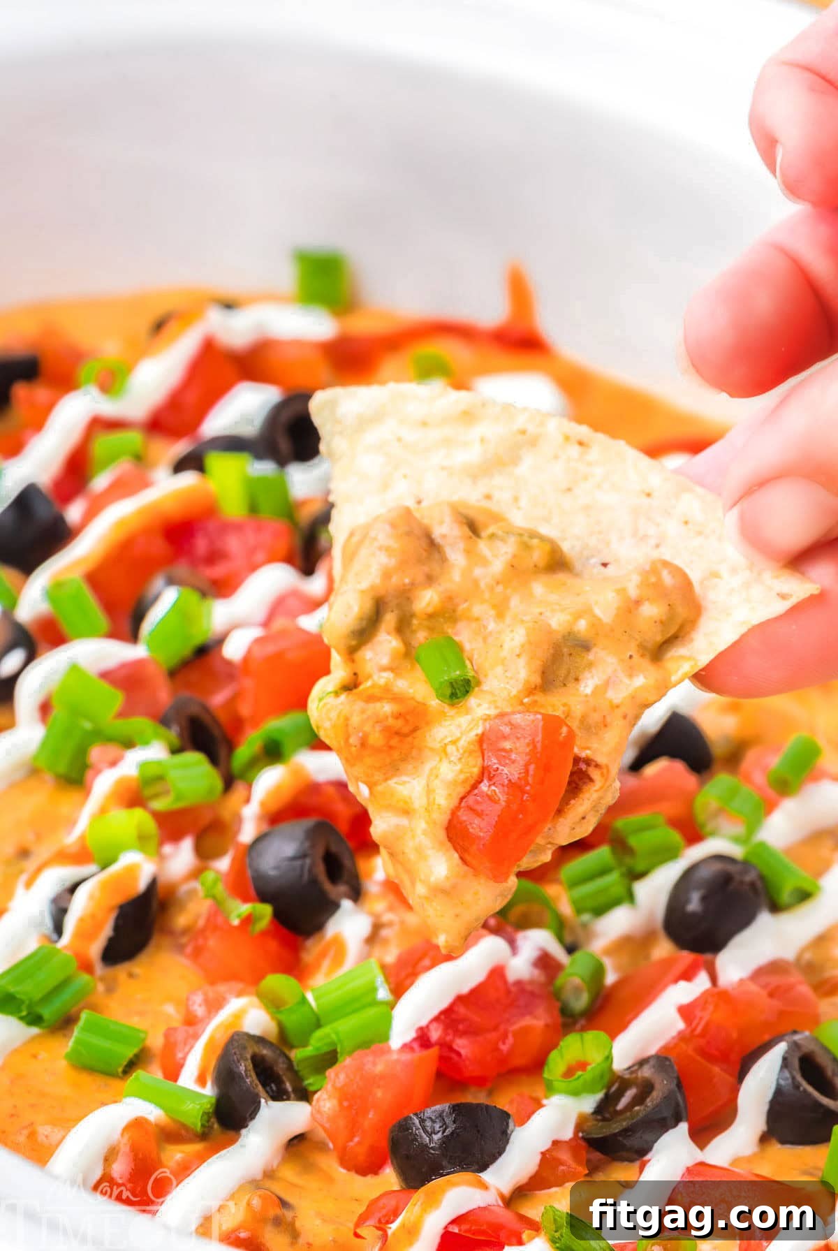 Warm and Cheesy Slow Cooker Taco Dip 7 A hand holding up a tortilla chip with crockpot taco dip on it.