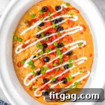 Warm and Cheesy Slow Cooker Taco Dip 9 Top down view of crockpot taco dip in a white crockpot. The dip has been topped with lots of taco toppings.