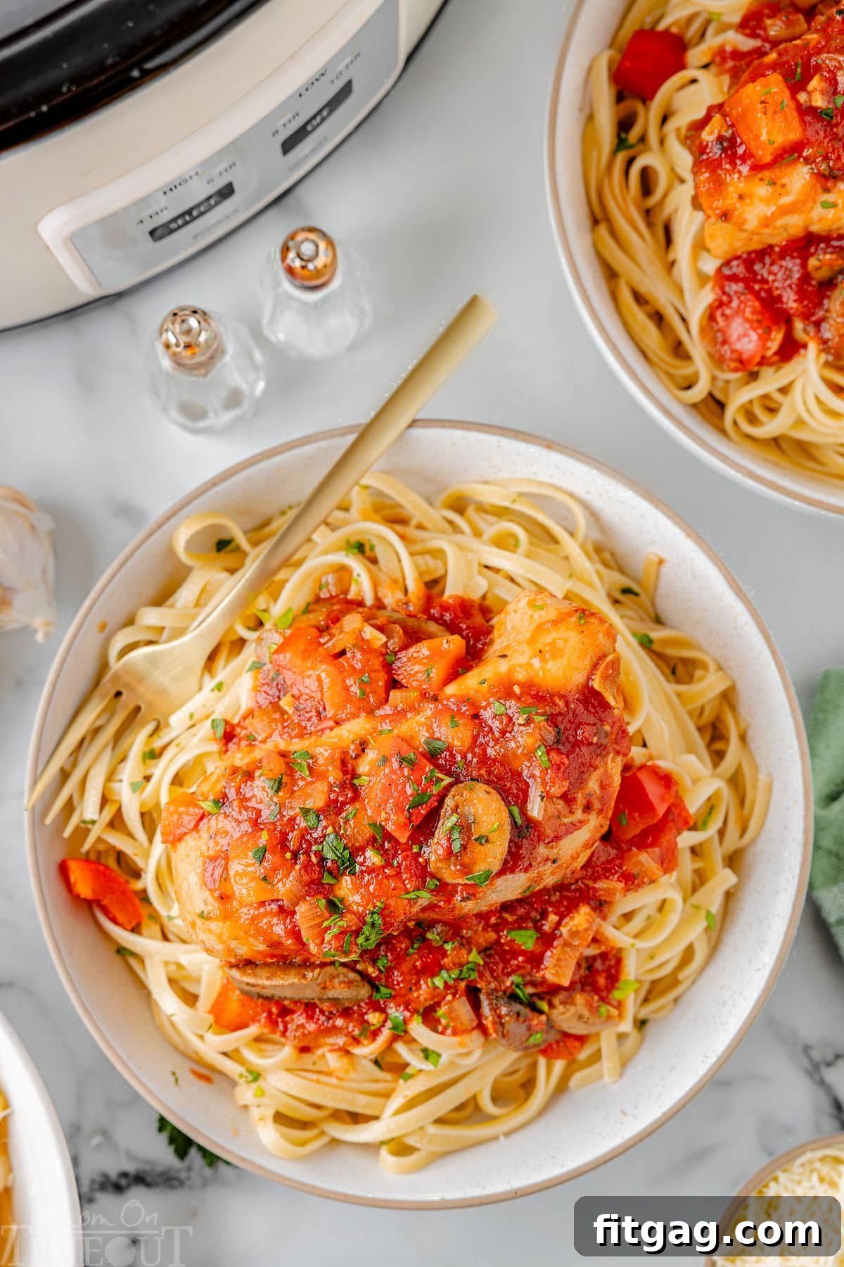 A delicious serving of Slow Cooker Chicken Cacciatore on a bed of perfectly cooked pasta, presented on a pristine white plate, with a matching white slow cooker visible in the background, hinting at its effortless preparation.