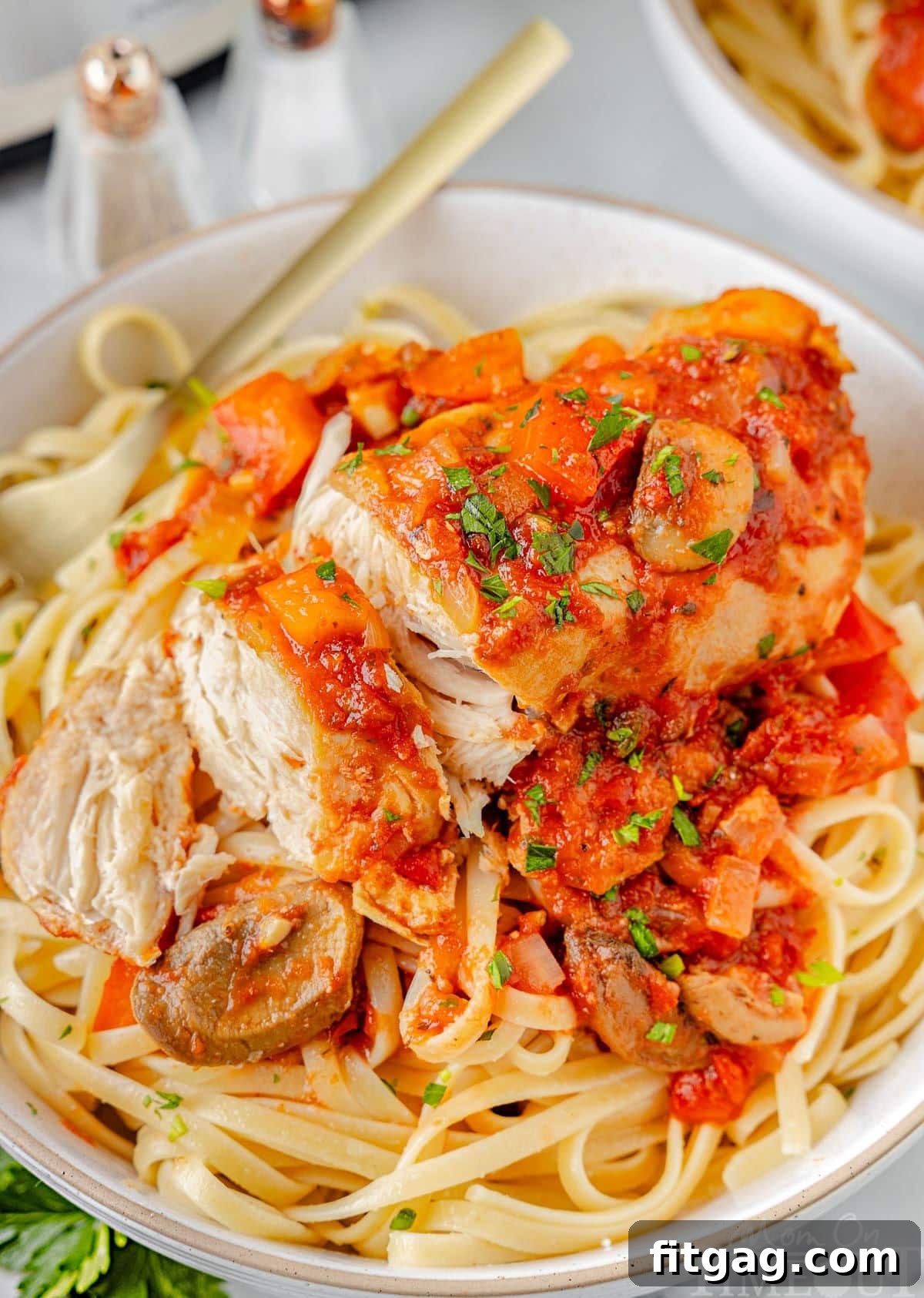Effortless Italian Chicken Cacciatore 3 A top down shot of chicken cacciatore sliced into pieces on a bed of pasta on a white plate.