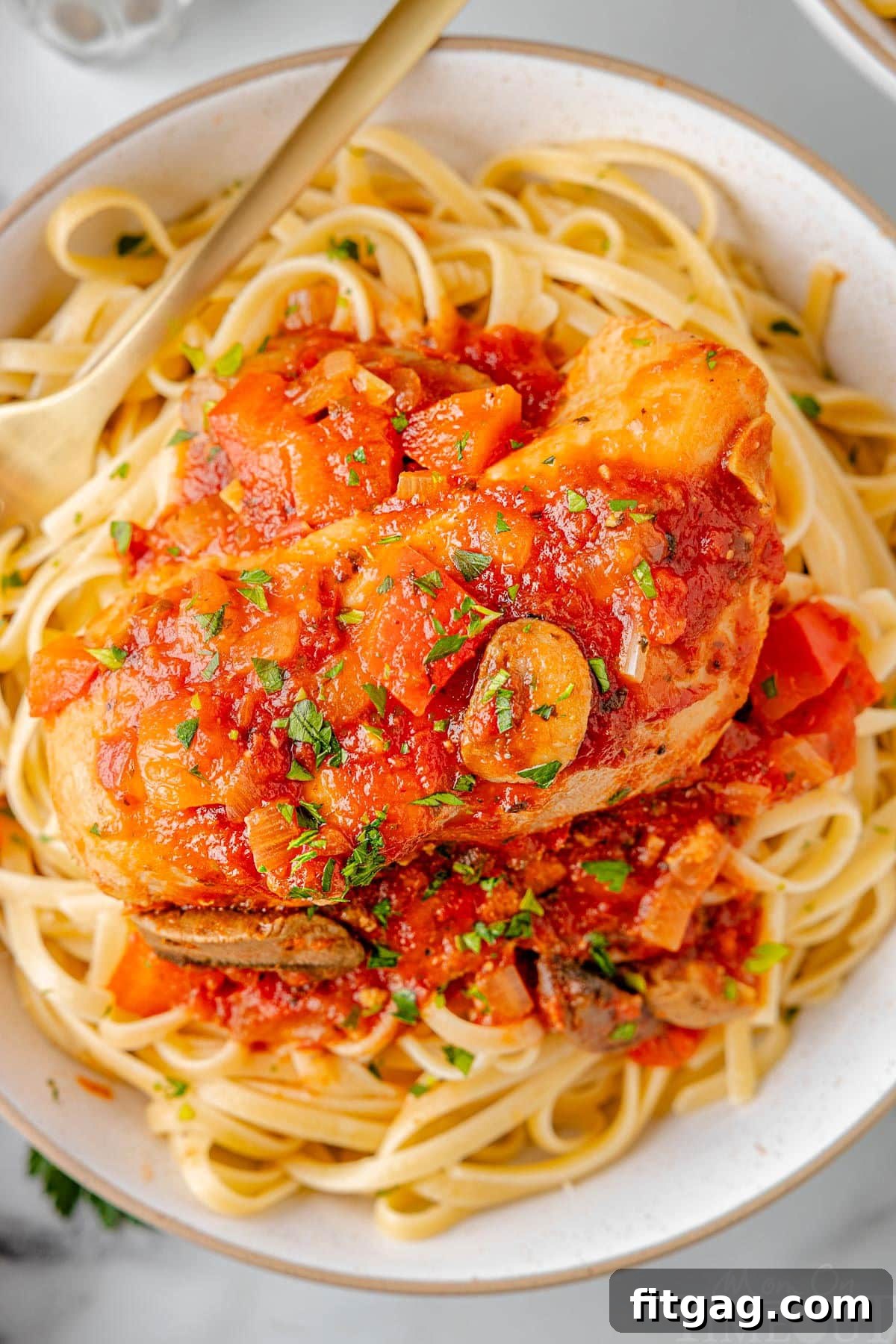 A top-down shot of a generous serving of Slow Cooker Chicken Cacciatore, perfectly arranged on a bed of pasta on a clean white plate, ready to be enjoyed.