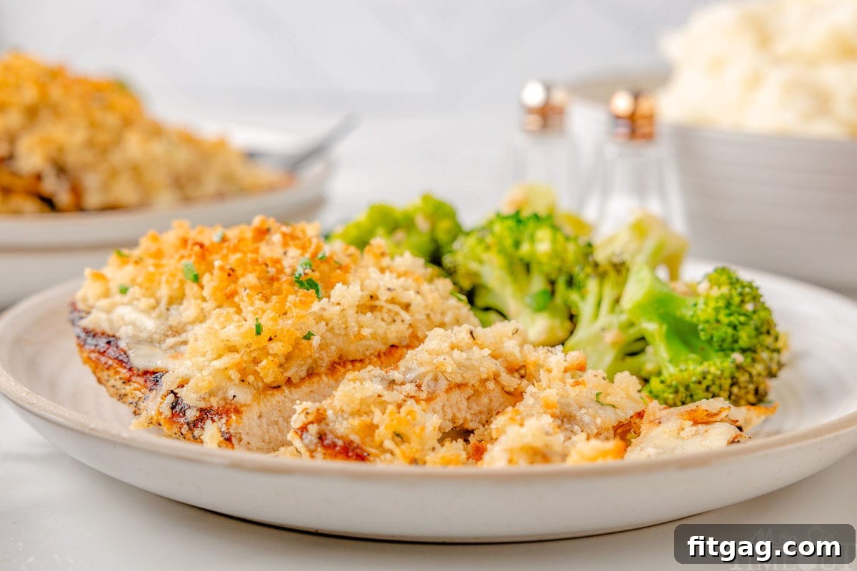 Wide shot of longhorn parmesan crusted chicken recipe on plate with broccoli on the backside of the plate. More chicken and mashed potatoes can be seen in the background.
