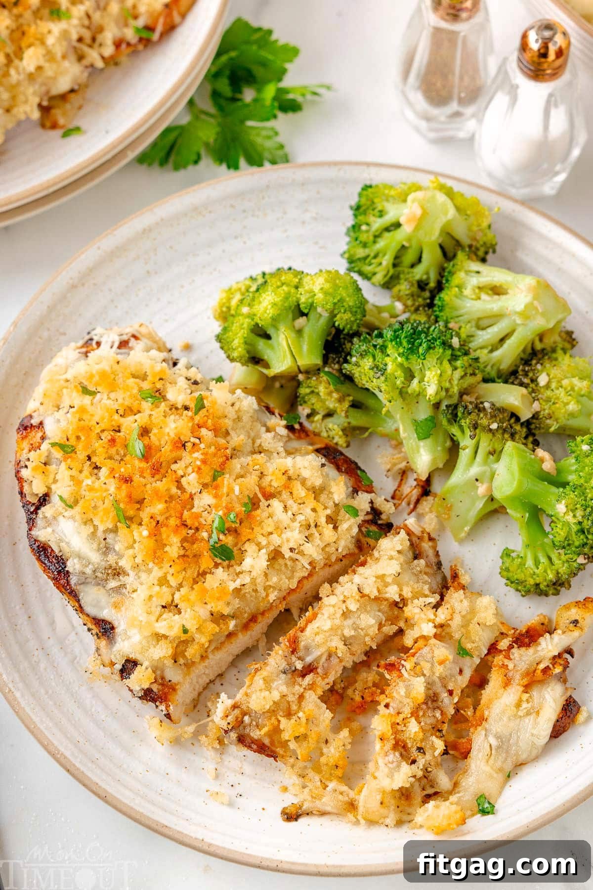 Top down view of Longhorn Parmesan Crusted Chicken plated with roasted broccoli on a round white plate. The crispy Parmesan and Panko topping is clearly shown and a few strips of chicken have been cut off the breast.