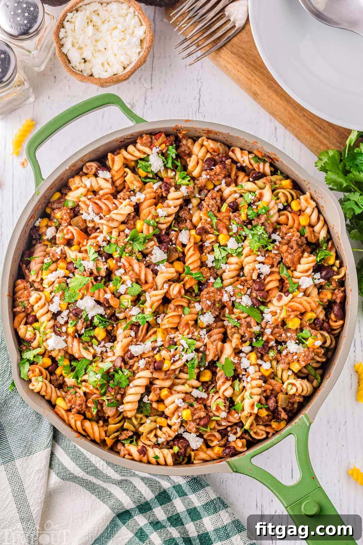 Top-down view of a vibrant green skillet brimming with taco pasta, beautifully garnished with fresh cilantro and crumbled queso fresco.