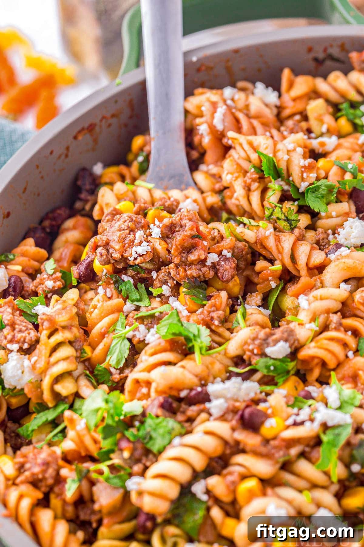 A close-up view of vibrant taco pasta being scooped from a skillet, showcasing its rich texture and colorful ingredients.