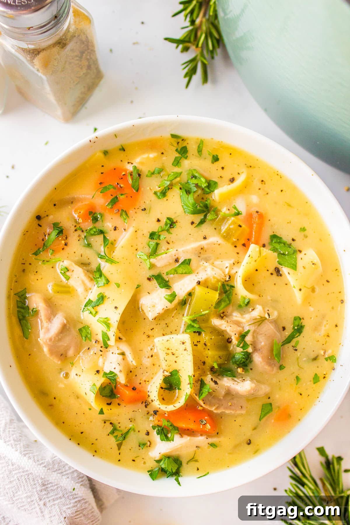 A top down shot of a white bowl of creamy chicken noodle soup, garnished with fresh dill and parsley.