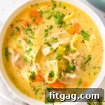 A top down shot of a white bowl of creamy chicken noodle soup garnished with fresh parsley.