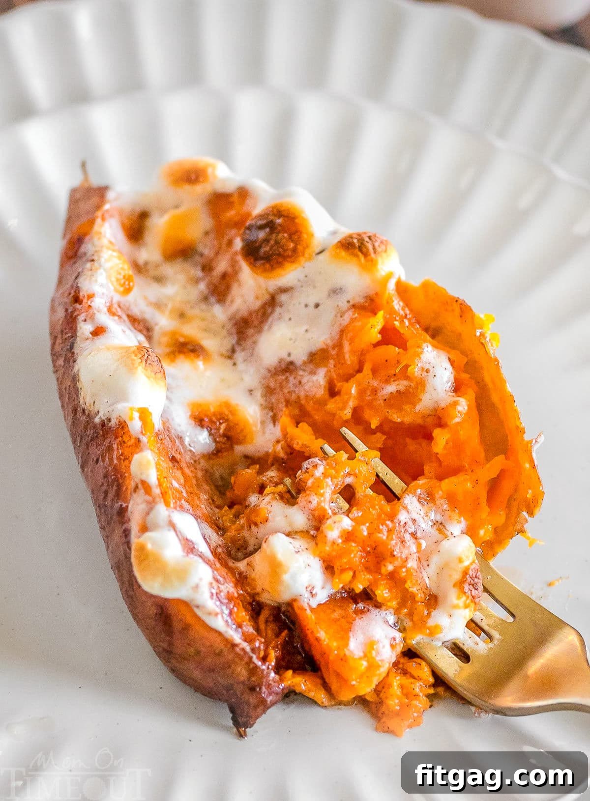 A twice baked sweet potato on a white plate with a gold fork in the potato.