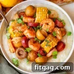Shrimp boil in a bowl served with grits. The bowl is sitting next to a sheet pan with the rest of the shrimp boil.