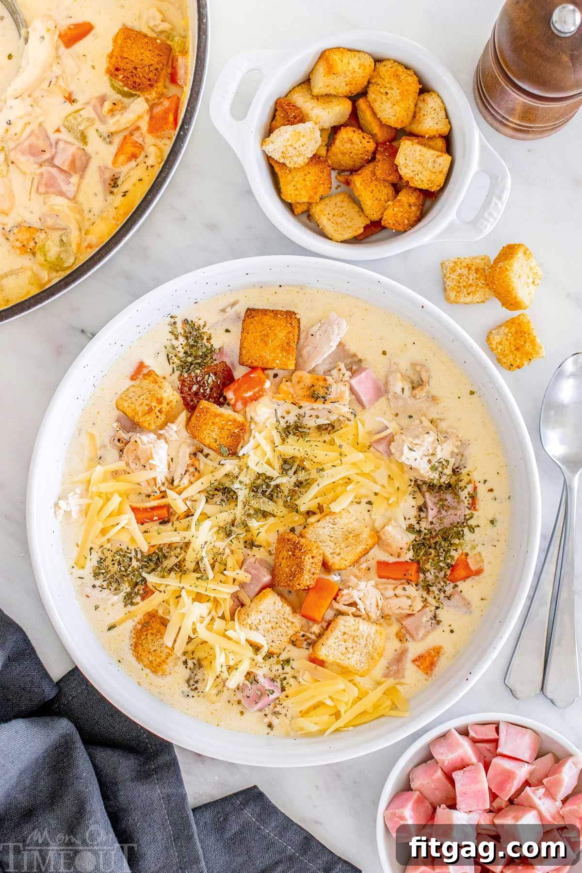 A top-down shot of a generous serving of creamy Chicken Cordon Bleu Soup in a white bowl, garnished with fresh herbs.