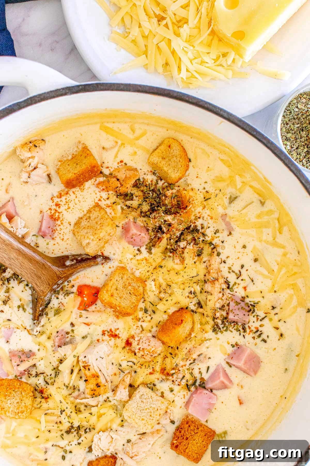 A top-down shot of Chicken Cordon Bleu Soup simmering in a rustic Dutch oven with a wooden spoon, showcasing its rich texture.