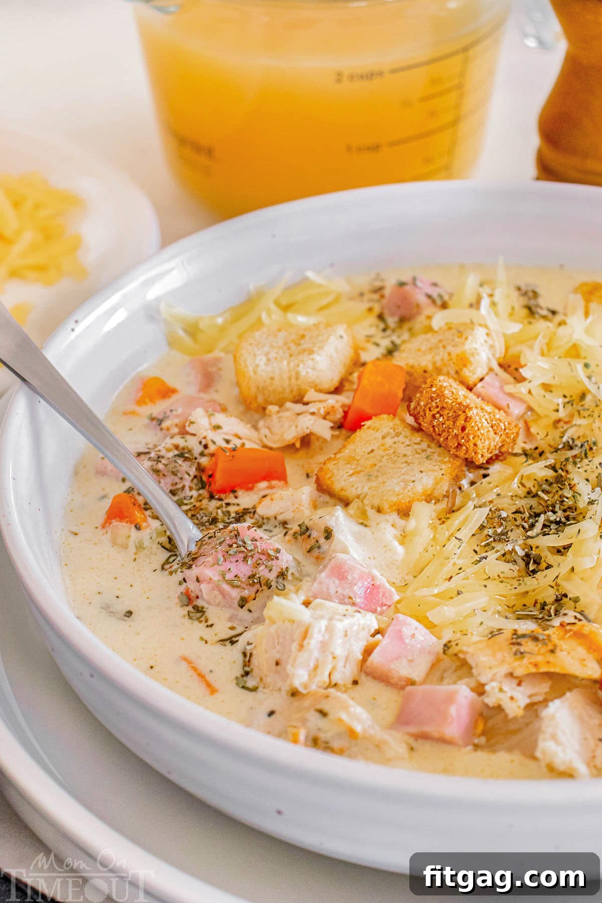 A close-up photo of Chicken Cordon Bleu Soup in a white bowl, with a spoon resting in it, highlighting the creamy texture and tender ingredients.
