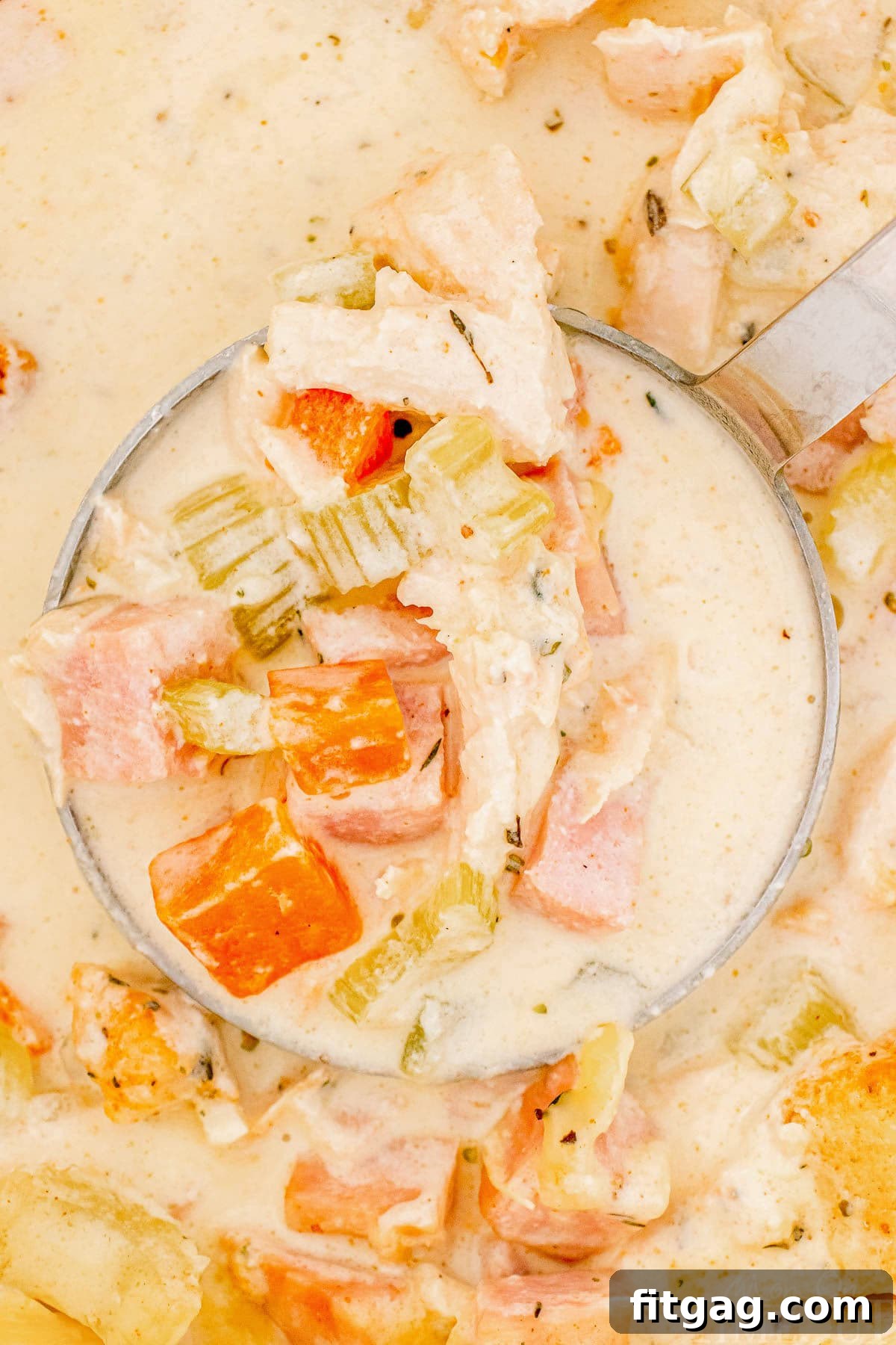 A ladle holding a scoop of creamy Chicken Cordon Bleu Soup, invitingly showing off the chicken, ham, and melted cheese.