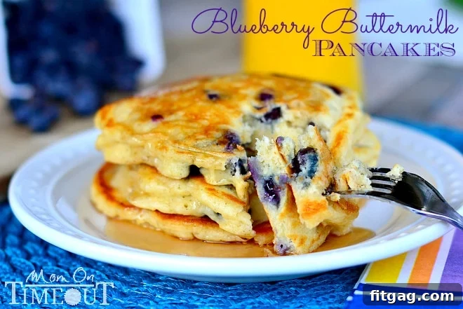 A beautiful stack of Blueberry Buttermilk Pancakes on a white plate with golden syrup, presented on a vibrant blue placemat.
