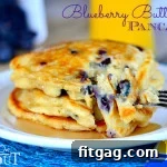 A stack of Blueberry Buttermilk Pancakes on a white plate with syrup on a blue placemat.