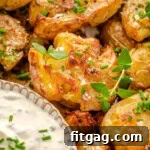 Close up of smashed potatoes on a plate garnished with chives and thyme sitting next to a small bowl of dip.