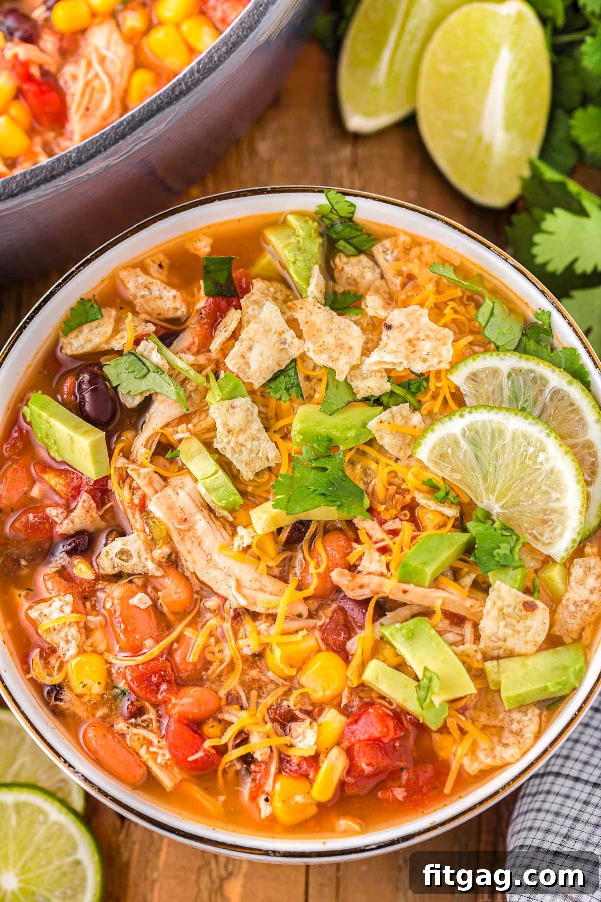 A top down shot of chicken taco soup in a bowl with lime slices next to the bowl.