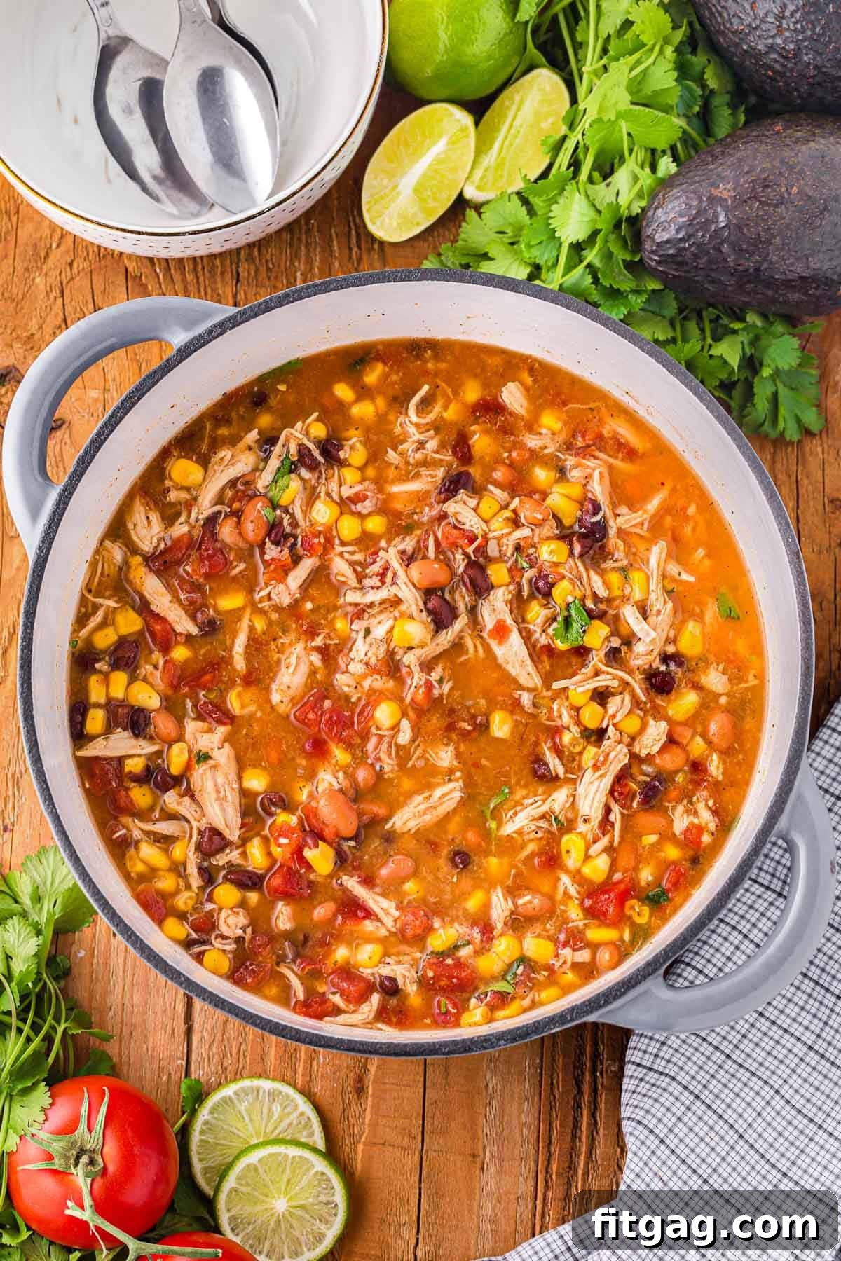 A top down shot of chicken taco soup in a dutch oven with garnishes and bowls on the table next to it.