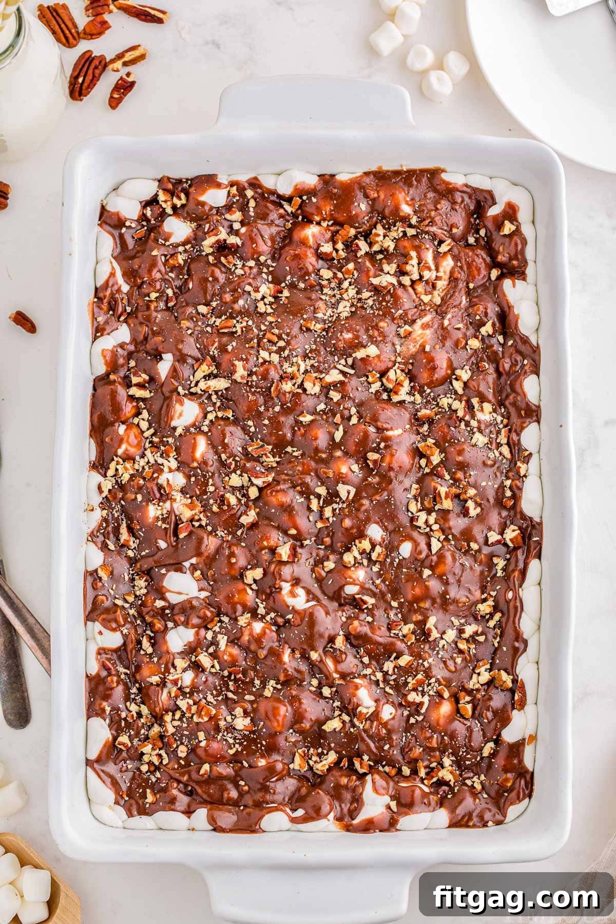 Riverbend Chocolate Dream 3 A captivating top-down view of a perfectly baked Mississippi Mud Cake, resting in a pristine white baking dish, ready to be sliced and served. A scattering of whole pecans artfully arranged next to the dish hints at the delicious nutty crunch within.