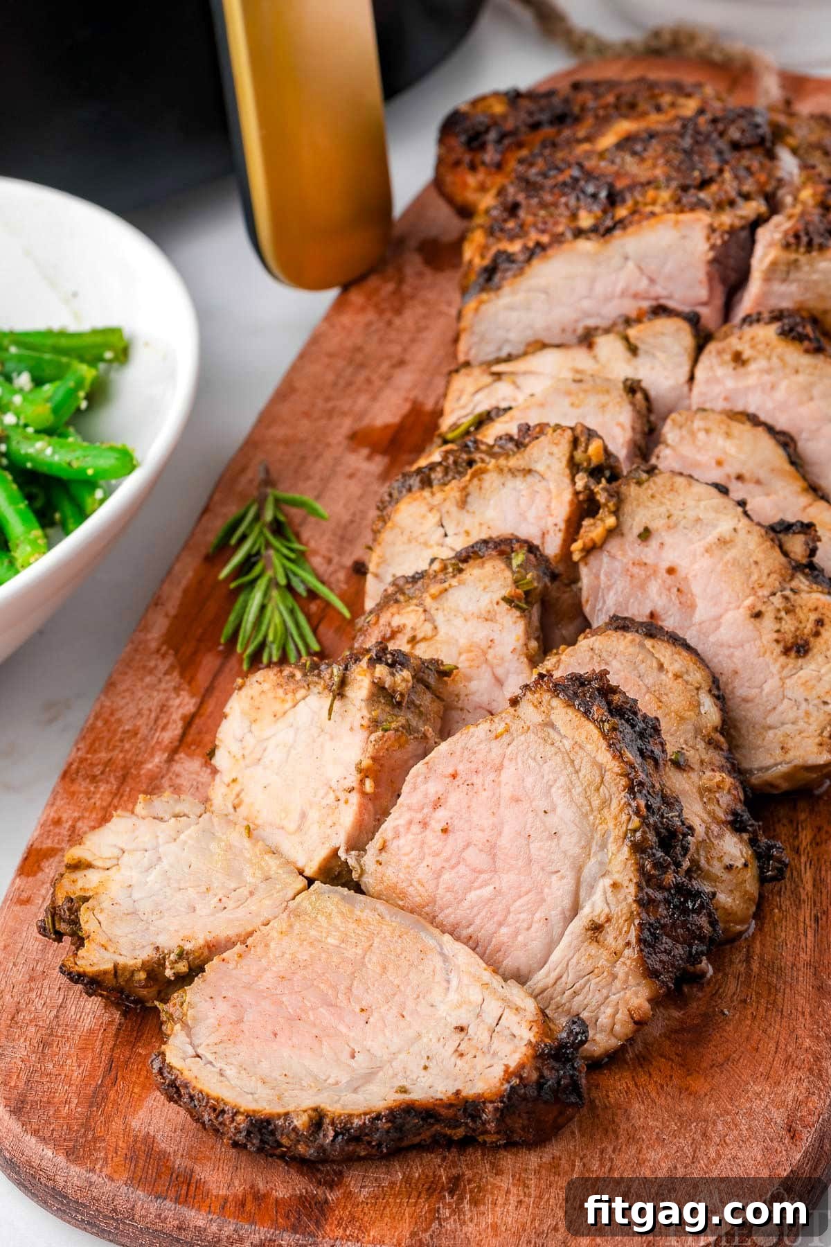 Perfectly Tender Air Fryer Pork Tenderloin 2 Air fryer pork tenderloin sliced into medallions on a wooden cutting board with an air fryer in the background.