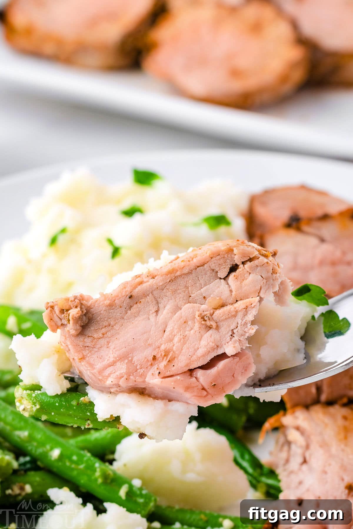 Perfectly Tender Air Fryer Pork Tenderloin 6 A fork lifting a piece of pork tenderloin from a plate, accompanied by mashed potatoes and green beans.