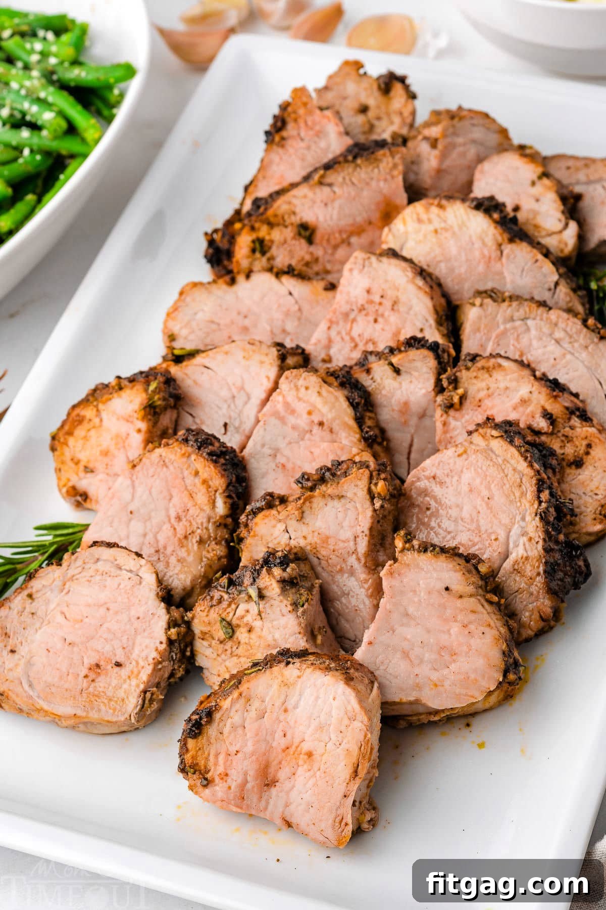 Perfectly Tender Air Fryer Pork Tenderloin 7 Slices of air fryer pork tenderloin arranged on a white rectangular platter, ready to be served.