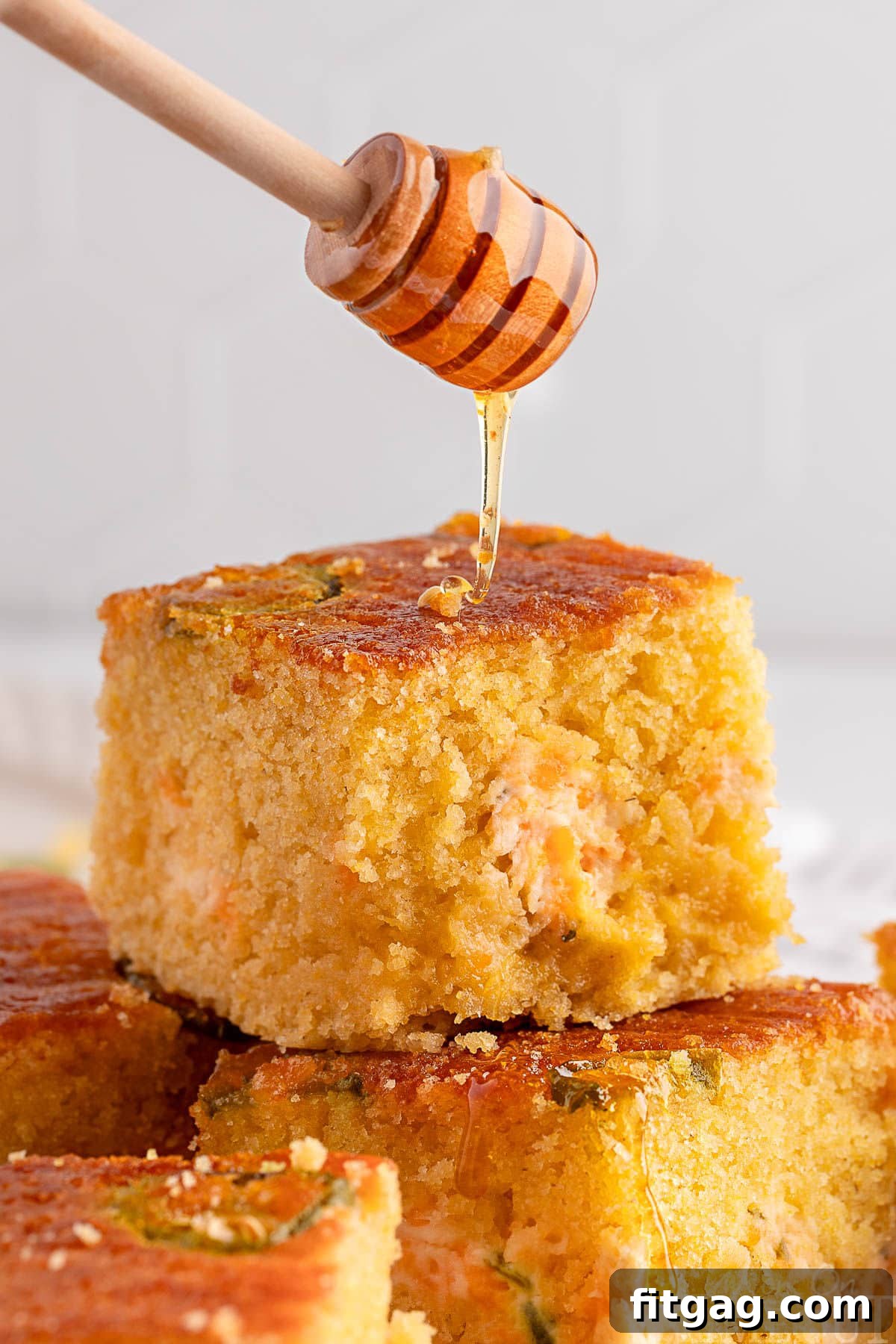 Spicy Cornbread Kick 5 Jalapeno cornbread recipe cut into squares and stacked on each other. Honey is being drizzled over the top of the cornbread.