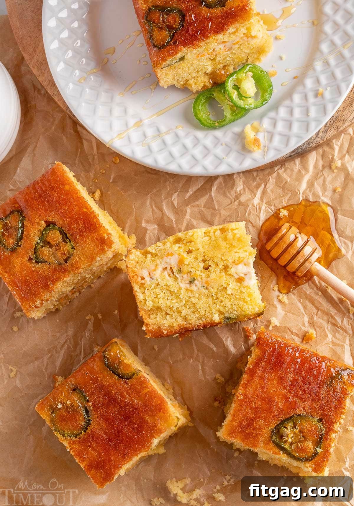 Spicy Cornbread Kick 6 Jalapeno cornbread cut into squares on brown parchment paper. One piece is on a white plate with two slices of jalapeno next to it.