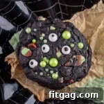 Monster Halloween Cookies stacked on brown parchment and black web design plate. Cookies have candy eyes and green sugar pearls for decoration.