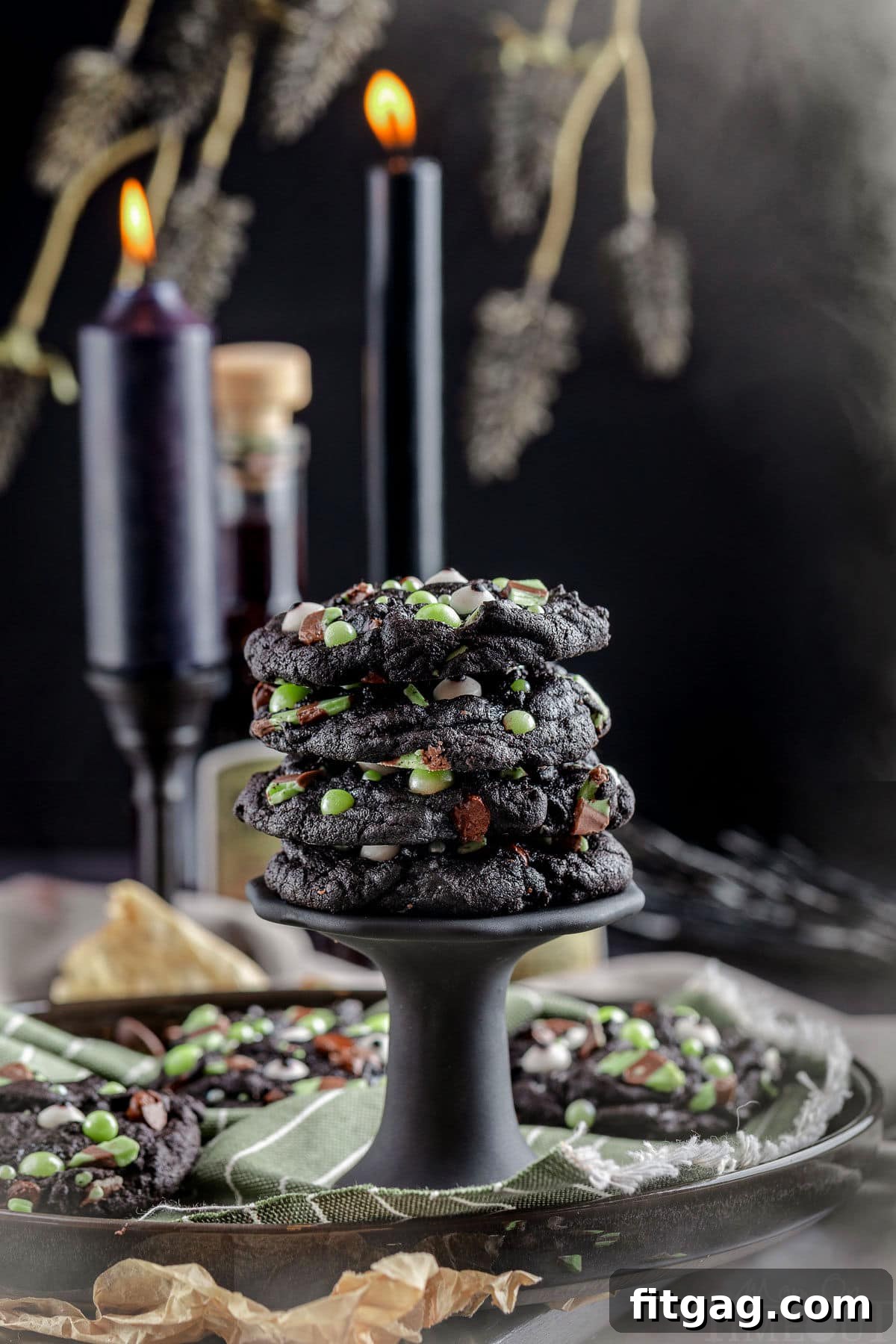 A stack of Halloween monster cookies on a black stand. Black candles and branches are in the background.