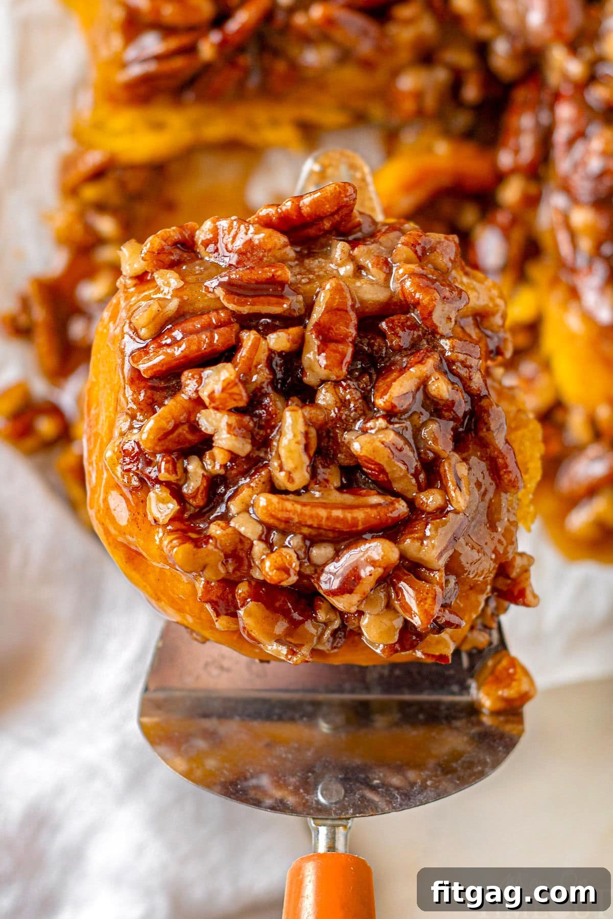 A freshly baked pumpkin sticky bun being gently lifted from a cutting board, revealing its warm, gooey caramel and pecan topping, ready to be savored.