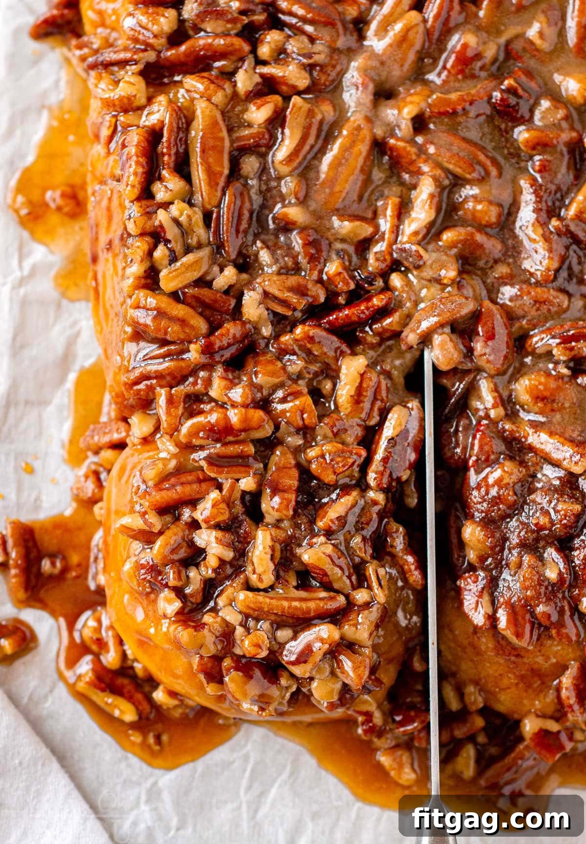 An overhead view of a pumpkin sticky bun being sliced away from the rest on a parchment-lined cutting board, revealing its gooey layers and caramelized pecans.