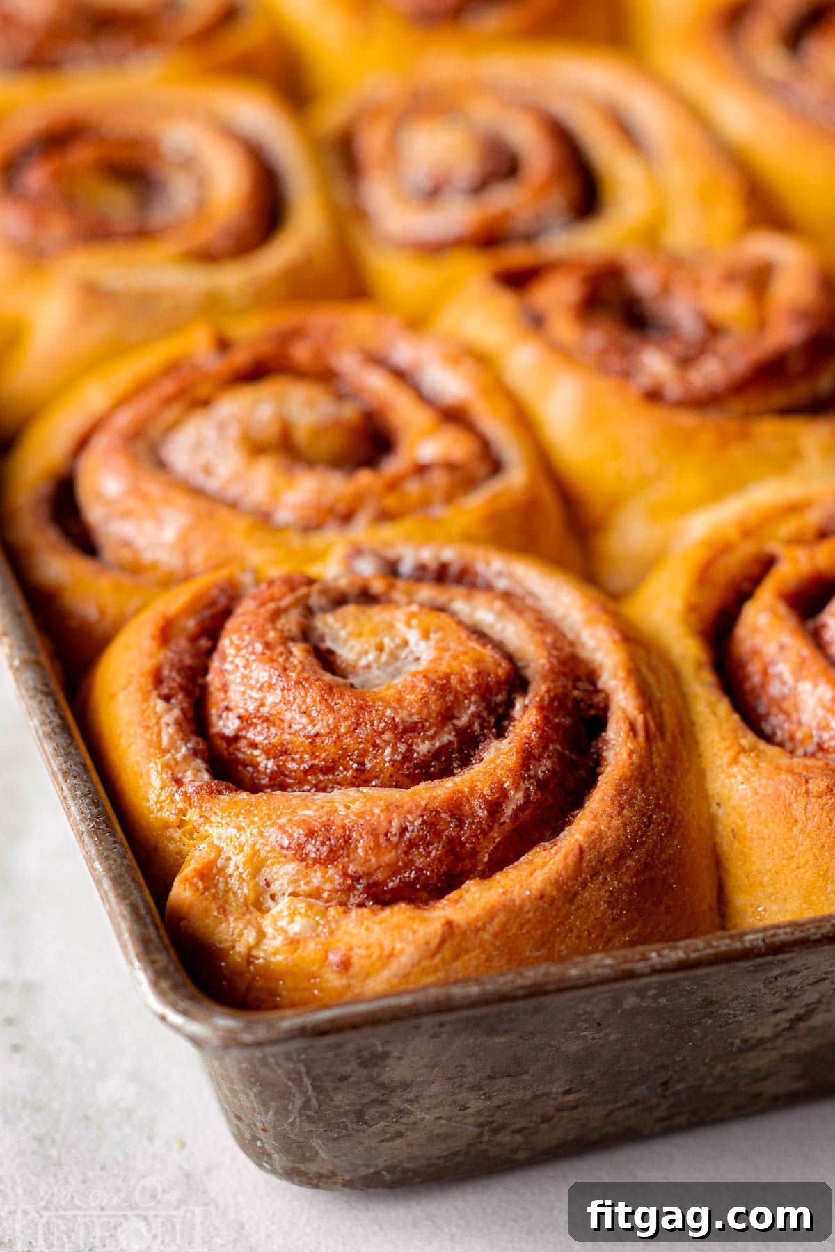 Baked pumpkin sticky buns still in the baking sheet, their tops golden and the caramel sauce bubbling around them, ready to be flipped and served.
