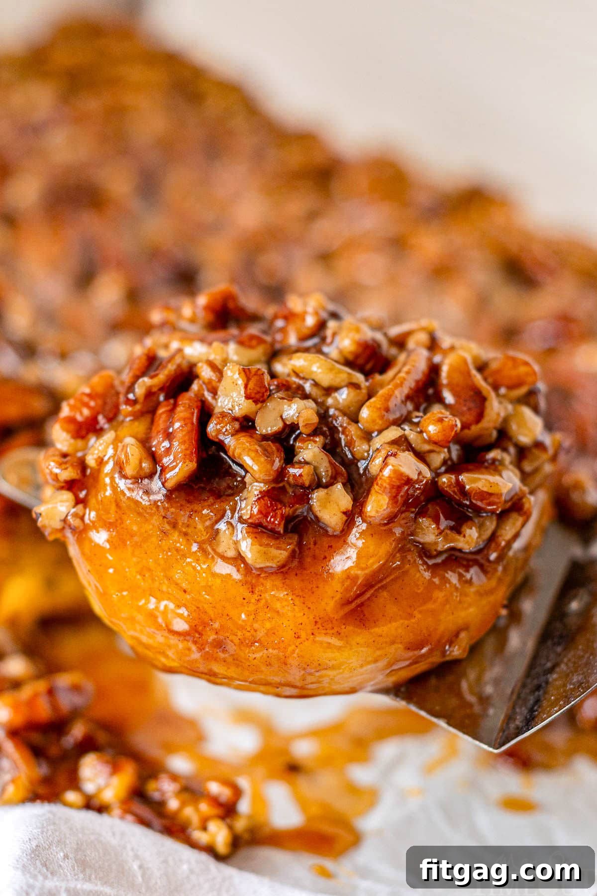 A perfectly baked pumpkin sticky bun, generously coated in glossy caramel and crunchy pecans, is served on a cutting board, ready for enjoyment.