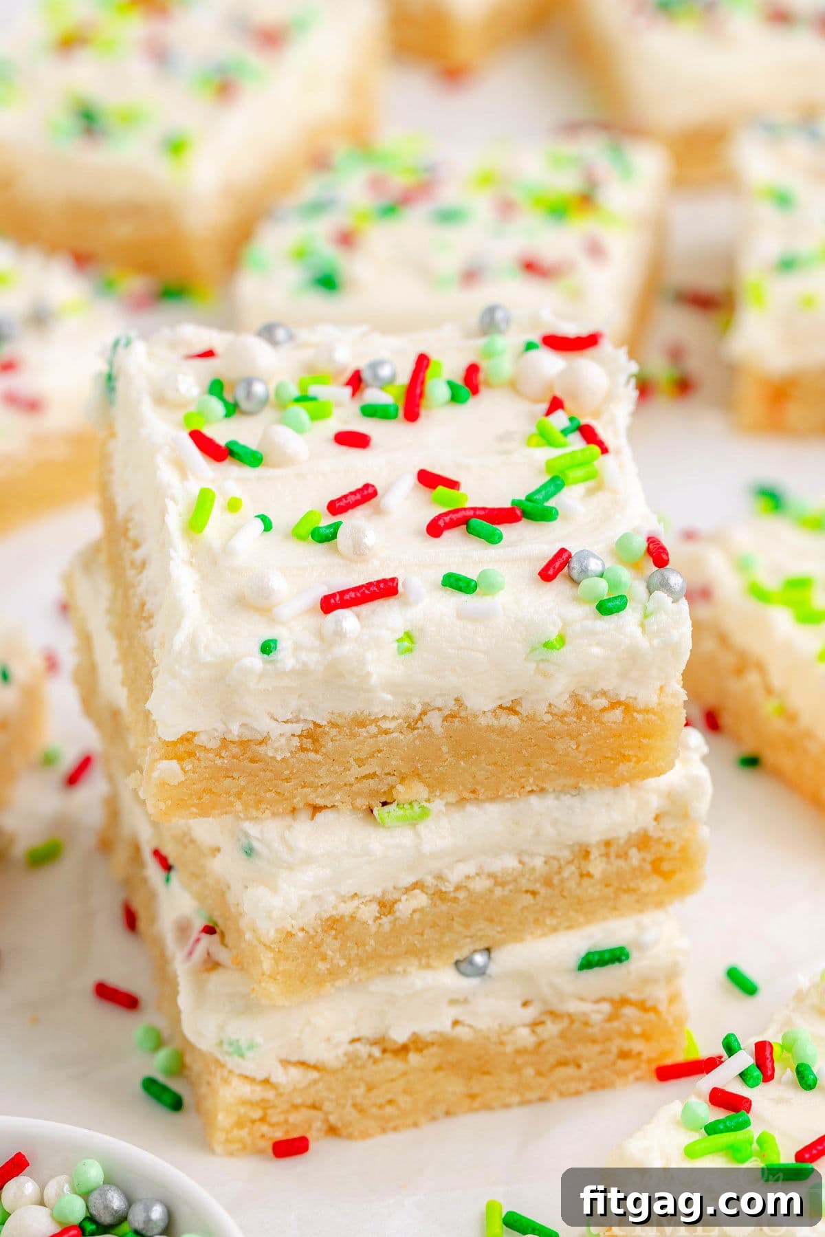Festive Frosted Sugar Cookie Bars 2 Three Christmas Sugar Cookie Bars in a stack with more bars in the background, showcasing their festive appearance and tempting frosting.