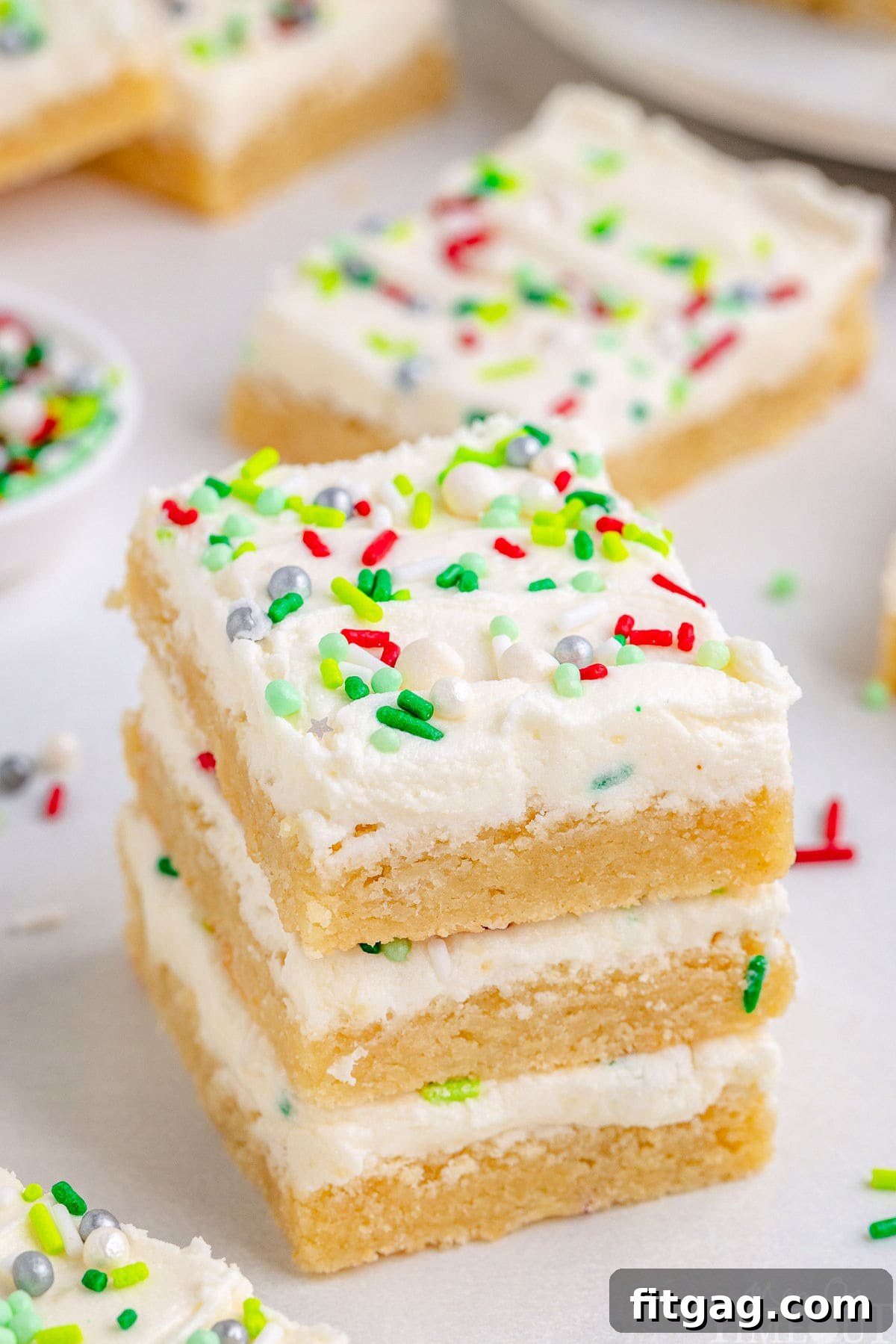 Festive Frosted Sugar Cookie Bars 7 Three Christmas Sugar Cookie Bars in a stack, with more bars in the background, showing their uniform shape and appealing frosting.