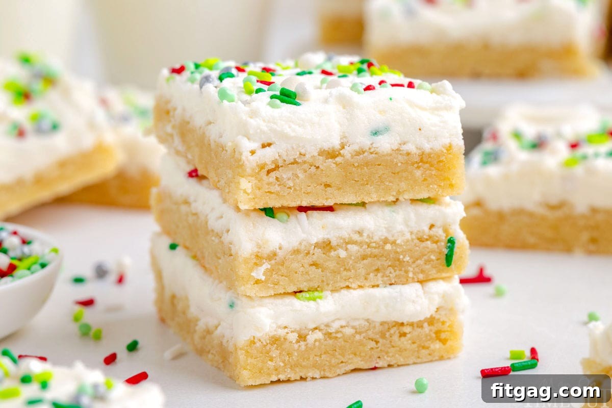 Festive Frosted Sugar Cookie Bars 8 Three Christmas Sugar Cookie Bars stacked with more bars blurred in the background, highlighting the focus on the perfectly frosted and sprinkled treats.