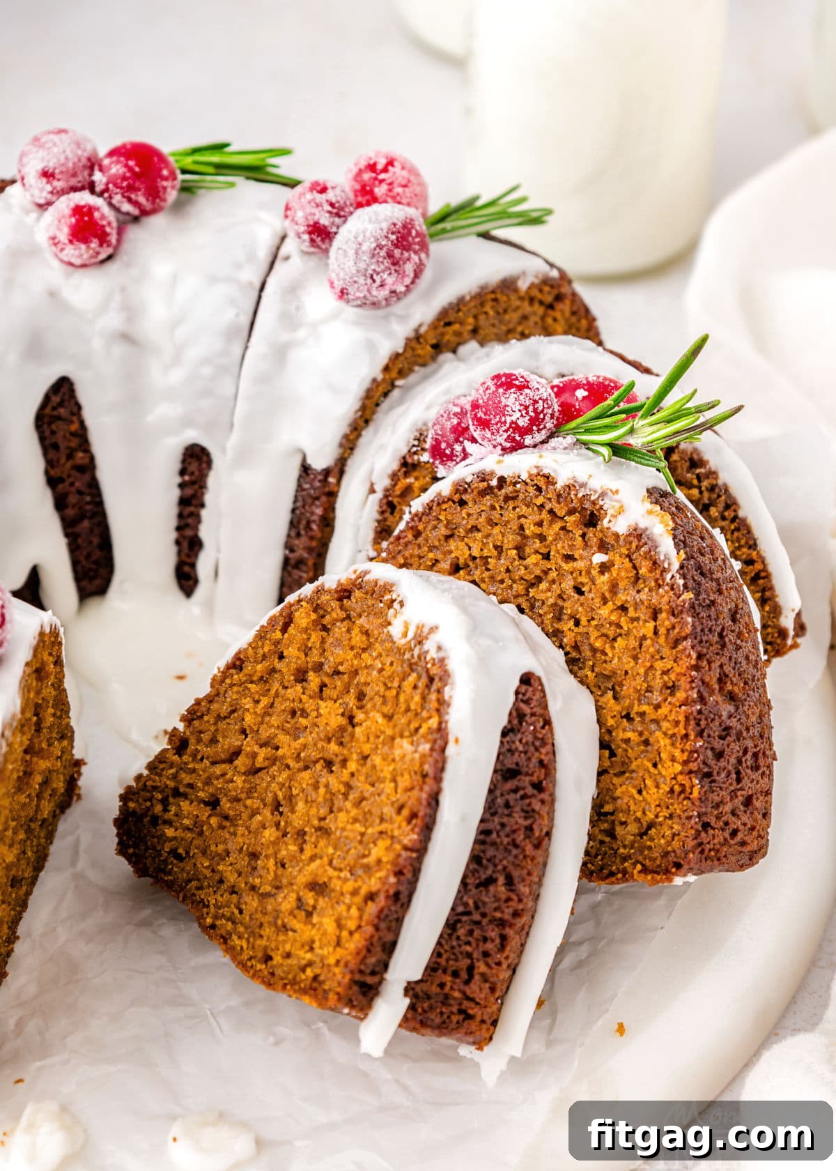 A gingerbread bundt cake with slices taken out of it. The cake is on a white cake stand.