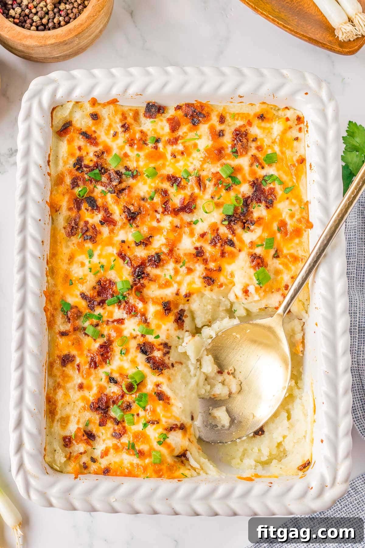 Homestyle Potato Perfection 3 Top down look at loaded mashed potato casserole in a white baking dish with a gold serving spoon resting in the dish where a serving has been removed.