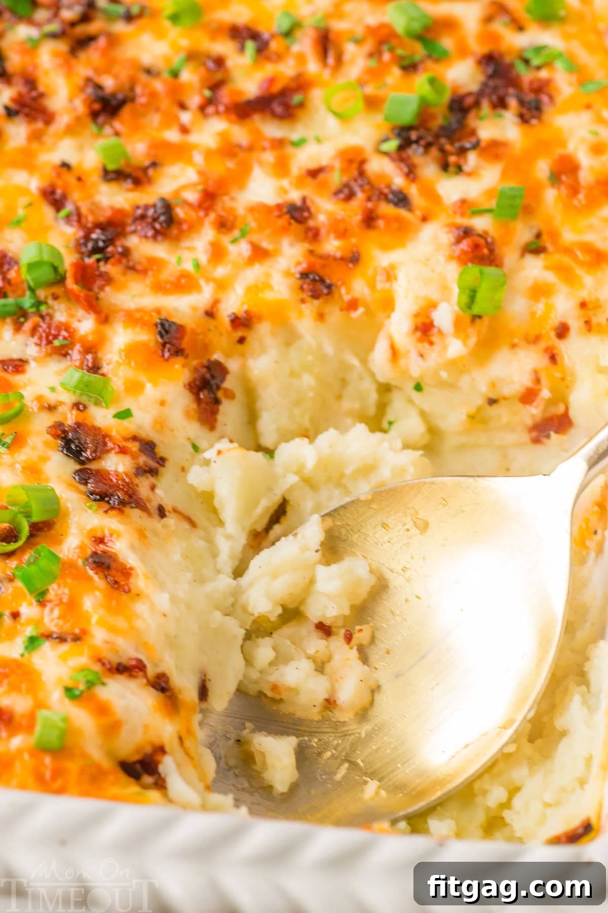 Homestyle Potato Perfection 6 Top down look at loaded mashed potato casserole recipe in a white baking dish with a gold serving spoon resting in the dish where a serving has been removed.