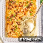 Homestyle Potato Perfection 8 Top down look at mashed potato casserole in a white baking dish with a gold serving spoon resting in the dish where a serving has been removed.