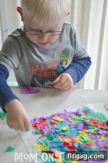 Child placing torn tissue paper onto a glue-covered wax paper