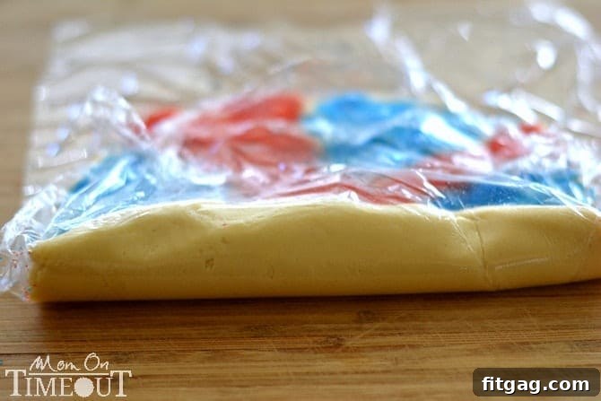 Rolled-up cookie dough log, neatly wrapped in plastic, ready for chilling before slicing into festive Red, White, and Blue Sparkler Cookies.