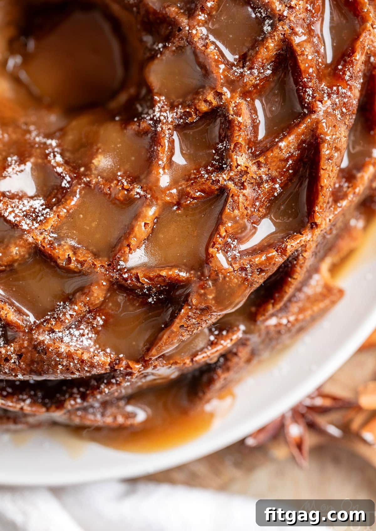 A top-down perspective showcases a beautifully golden Caramel Apple Bundt Cake resting on a elegant white cake plate. The glossy bourbon caramel glaze pools seductively into every curve and ridge of the bundt, hinting at its rich, sweet flavor and moist interior. Perfect for fall gatherings.