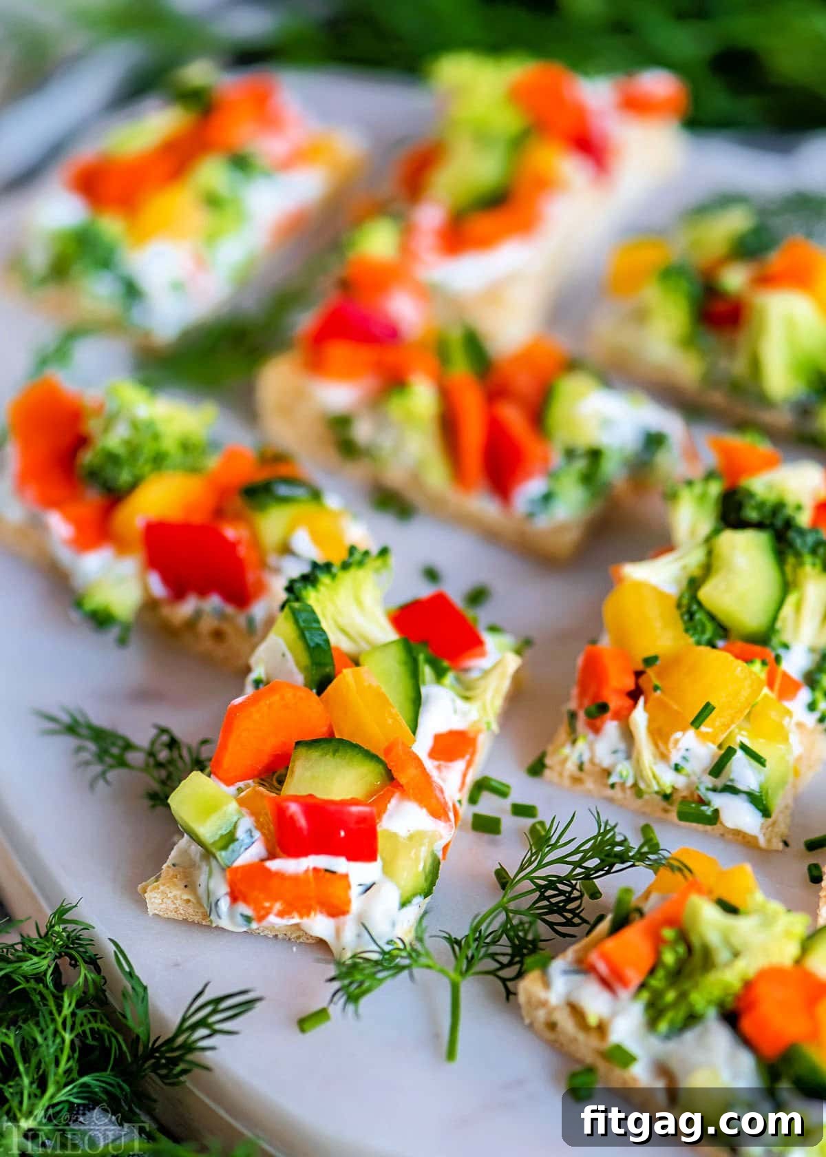 Party-Perfect Veggie Pizza Bites 2 Freshly cut veggie pizza rectangles on a marble board, garnished with vibrant dill sprigs, ready to serve as a light and crunchy appetizer.