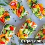 top down view of veggie pizza recipe assemble and cut into small pieces for serving. dill sprigs are scattered about on the marble cutting board.