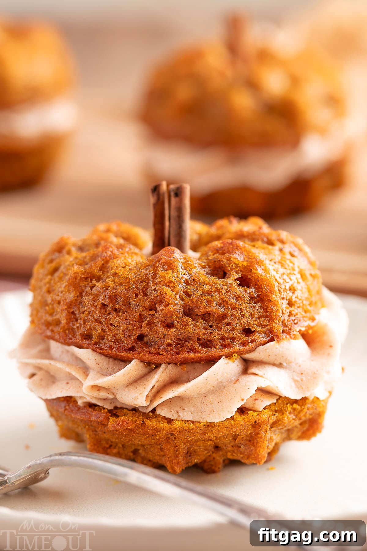 Mini pumpkin bundt cake made with two small bundts and sandwiched with cinnamon brown butter frosting. The stem is a cinnamon stick. The cake is sitting on a white plate with a fork.